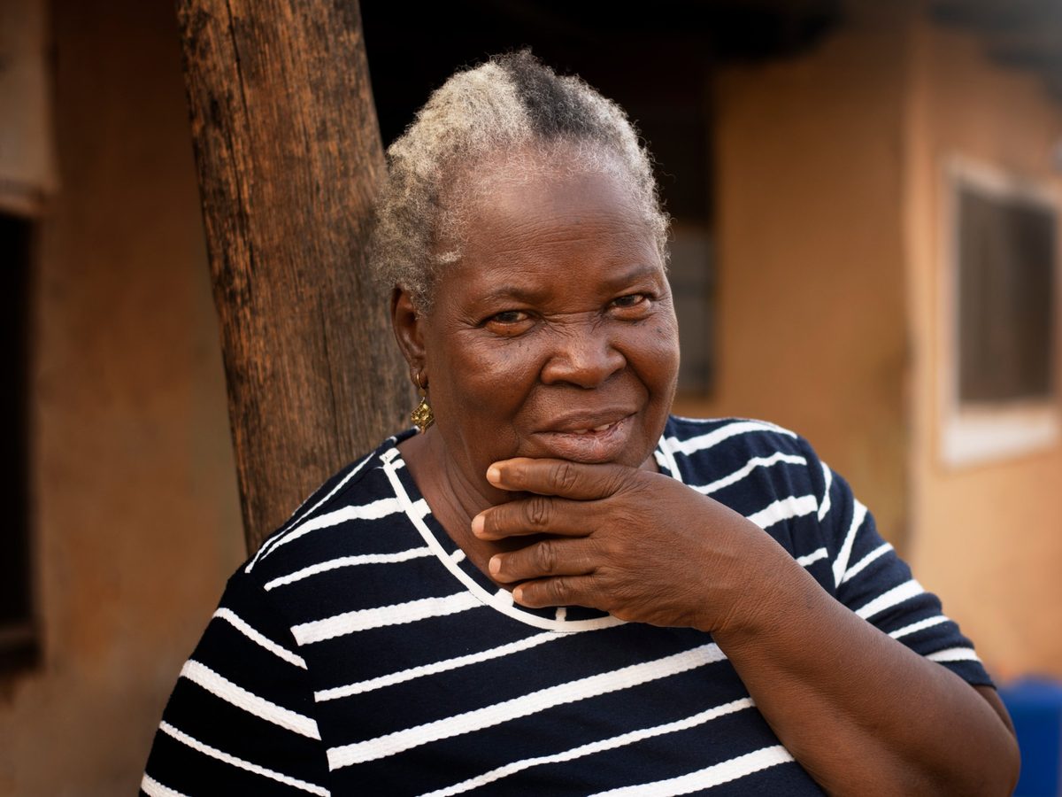 Une dame âgée souriante devant sa maison